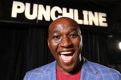 Yoshee, comedy teacher, smiling in front of the Punchline comedy club sign